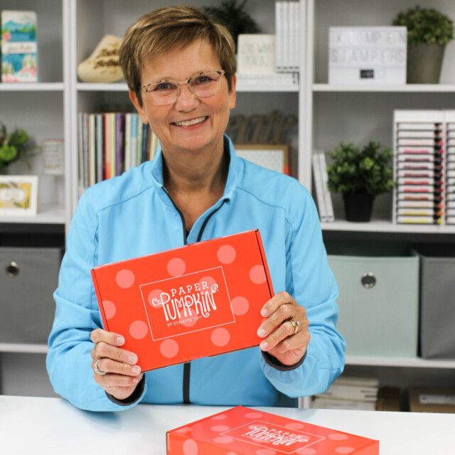 Picture of Jackie Bolhuis of Klompen Stampers standing at her crafting desk holding a Stampin' Up! Paper Pumpkin box.