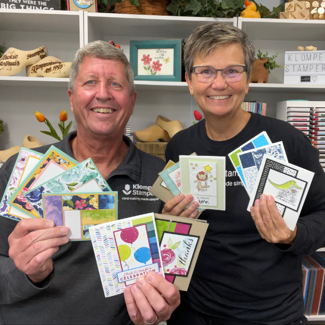 Jackie and Dave of Klompen Stampers holding four card making templates and eight completed cards made from following the templates from one of their template making videos.