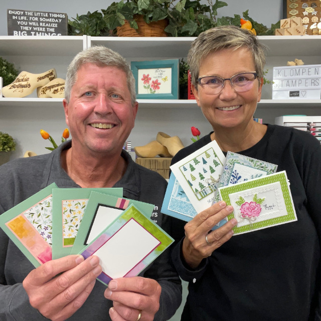 Jackie and Dave of Klompen Stampers holding four card making templates and four completed cards that were designed from the card templates.