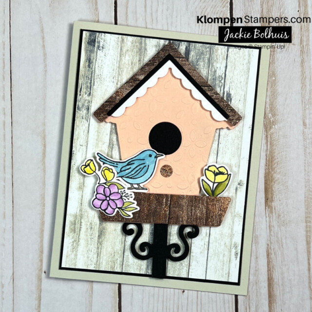 Elegant handmade card designed with the Stampin' Up! Bundle Country Birdhouse. Card has a light pink birdhouse that is standing on a pole, a blue bird, and yellow and purple flowers.