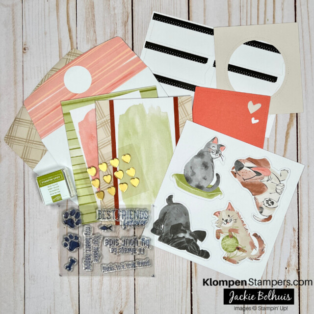 The contents of the all-inclusive By Your Side Card Kit from Stampin' Up! lying on a table. Contents include pre-printed card bases, envelopes, die-cut images of cats and dogs, a stamp set and small ink pad, and more paper layers.