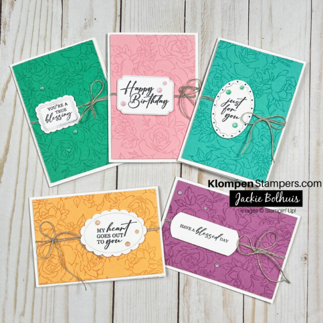 Five cards designed the same but each card is made using a different color. The cards have a large floral background layer, a small linen bow wrapped around it, and a die cut sentiment stamped on white.