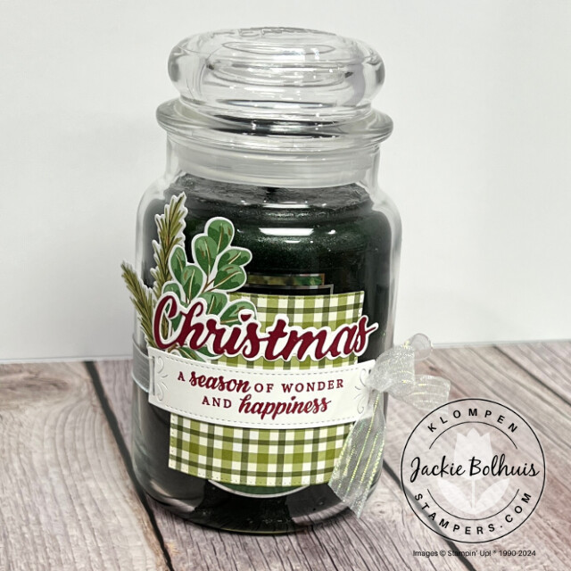 Handmade candle wrap for a Christmas gift for the never show up empty handed trend. Candle wrap is designed with Stampin' Up! products and is simple with green plaid paper, a Christmas sentiment, and a little holiday greenery, tied and attached to the candle with a bow.