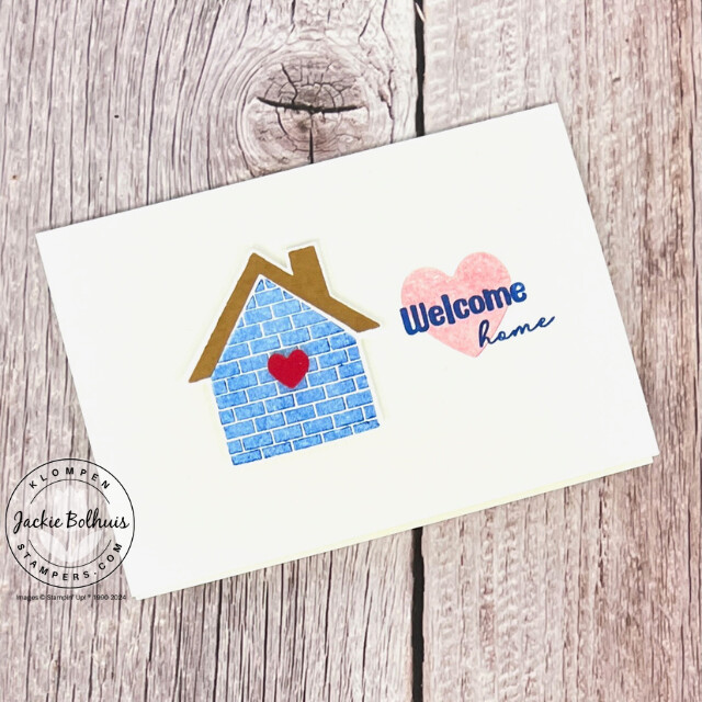 A military appreciation card that has a small blue brick home with a red heart on it, a large red heart stamped next to it with the words "welcome home" stamped in blue on top. 