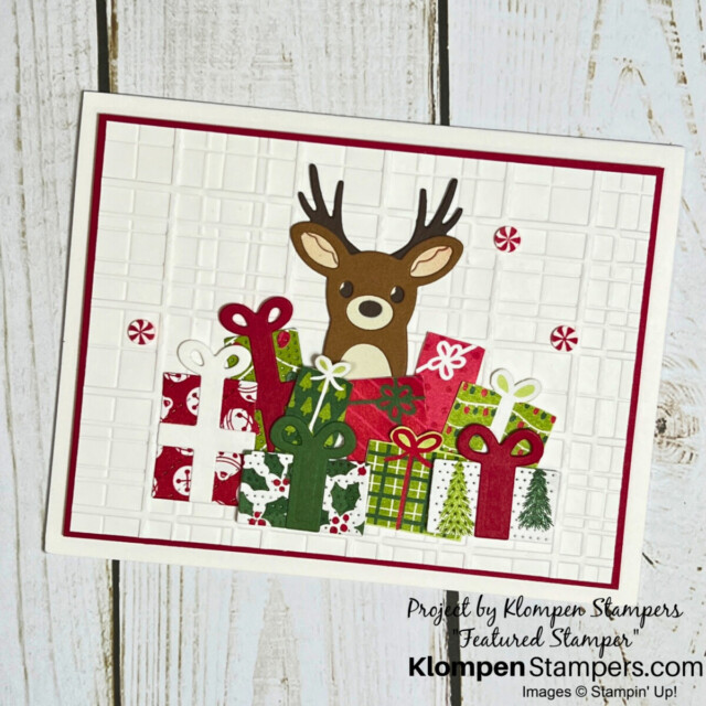 A handmade Christmas card with a reindeer in the background behind a pile of presents.