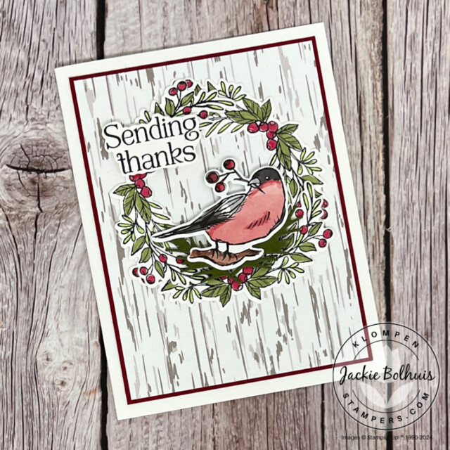 A thank you card that has winter birch background paper, a greenery wreath, and a die cut bird in the center.